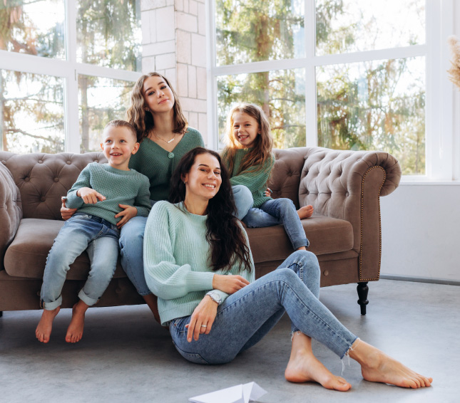 Mother sitting on the floor with three smiling children on a sofa