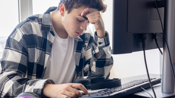 Teenage boy resting his head on his hand looking frustrated at a computer