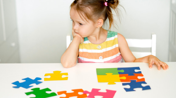 Young girl sitting at a table looking thoughtfully at colourful puzzle pieces