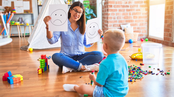 Woman holding up smiley and sad face drawings for a toddler during a learning and behaviour session