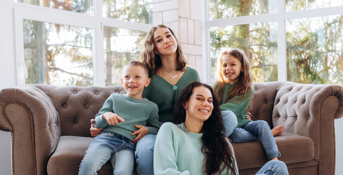 Mother sitting on the floor with three smiling children on a sofa