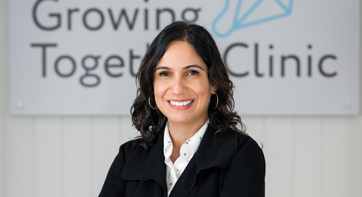 Dr Marium Rind smiling in front of the Growing Together Clinic sign